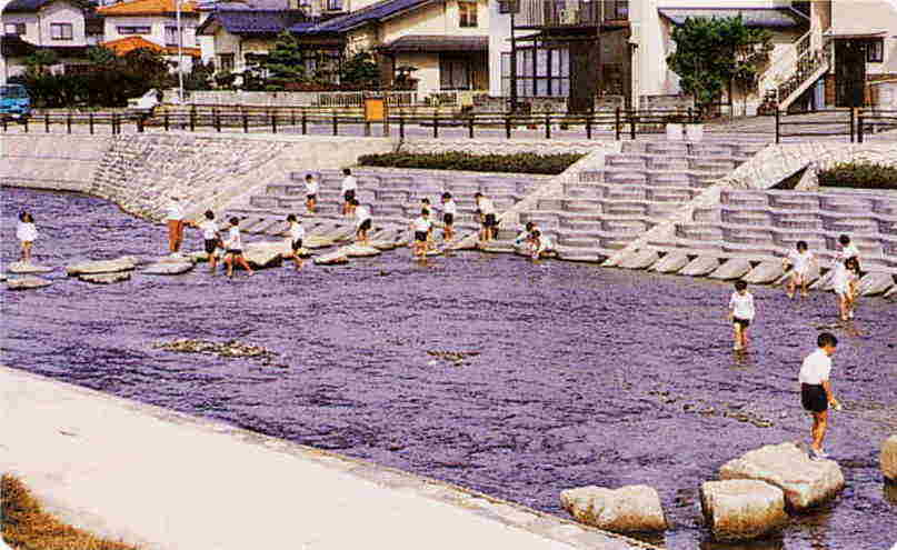 伏見川の階段護岸や飛び石で遊ぶ子ども達の写真
